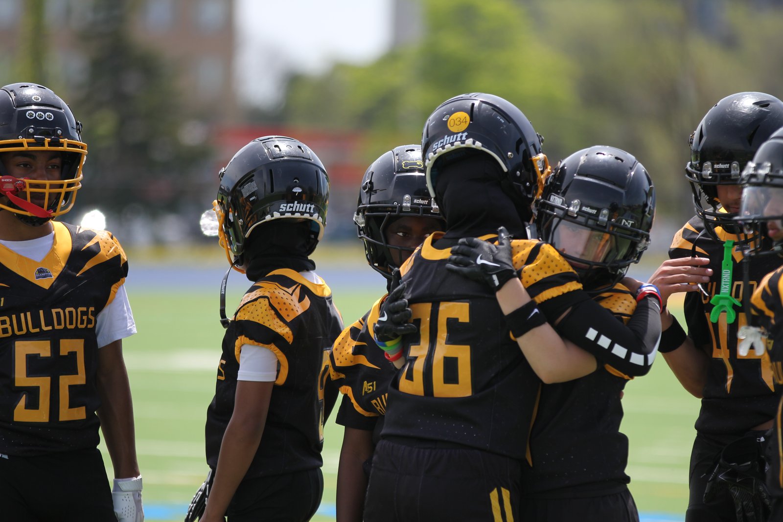 Brampton Bulldogs Bantam offensive linemen huddled close on the field, helmets touching, BULLDOGS reading clearly across one player's jersey