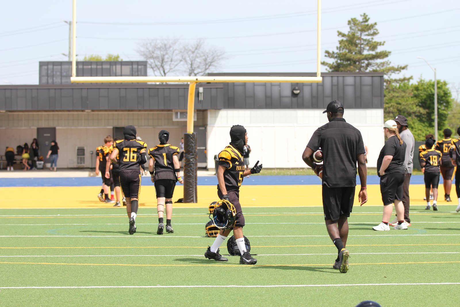 A coach and two Bulldogs Bantam players walking onto the field with a goalpost in the background
